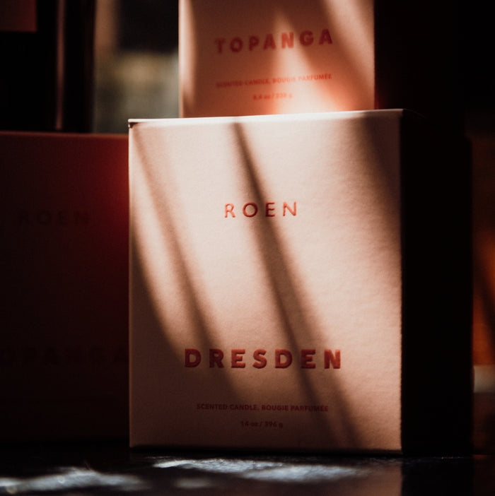 Candle boxes with 'Roen' and 'Dresden' branding on a dark background